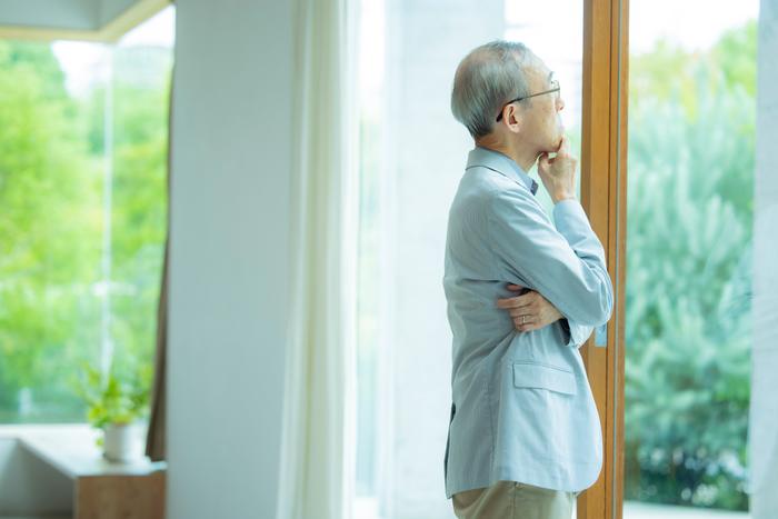 窓辺で実家のことを考えるシニア男性